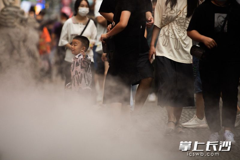 在太平老街，一位小朋友穿着长衣长裤在商家布置的雾气中玩耍。
