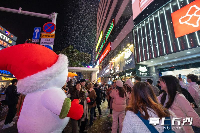 雪人玩偶与行人互动合拍，让长沙“第一场瑞雪”的仪式感更加具体和丰富。