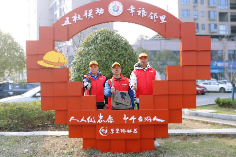 三名维修队员在集里桥社区“人人做志愿，个个做好人”标牌前合影。